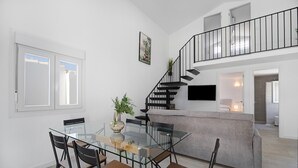 Ein modernes Interieur mit einem Glastisch, Stühlen, einem grauen Sofa, einer Treppe und einem Flachbildfernseher.