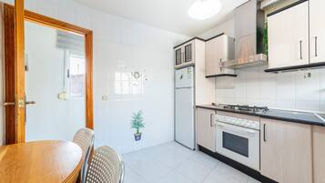 Una cocina con baldosas blancas, una mesa de comedor de madera, sillas, una estufa y alacenas.