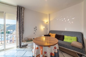A balcony with a view of buildings, a sofa with cushions, a table with a patterned tablecloth, and wall decorations.