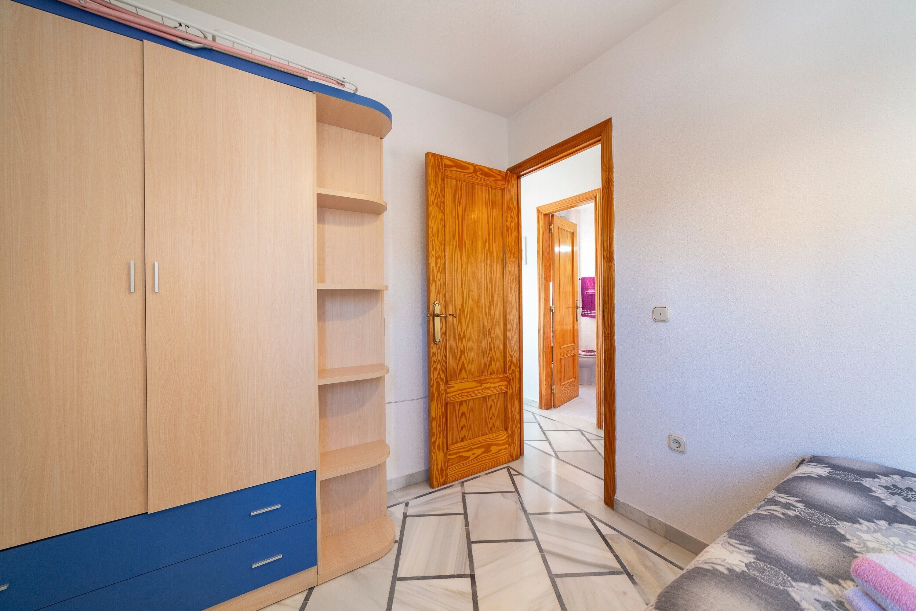 A bedroom with a bed, a wardrobe, a door, and a tiled floor.
