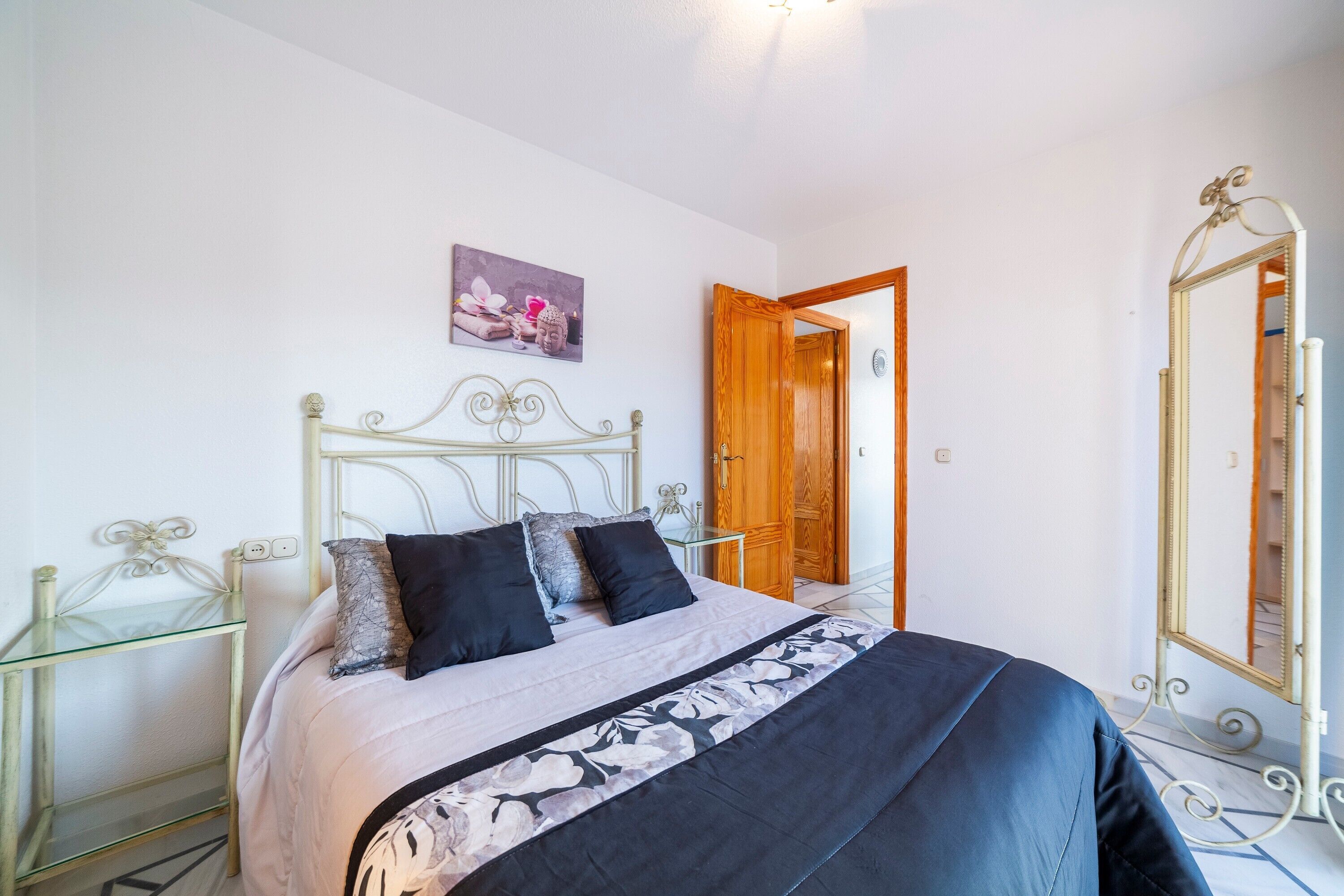 Een slaapkamer met een bed, een glazen bijzettafeltje, een houten deur en een spiegel.