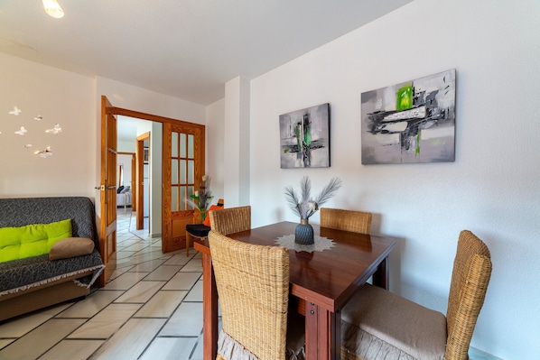 A dining area with a wooden table, wicker chairs, and artwork on the walls.