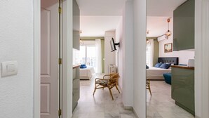 A hallway leading to a bedroom with a bed, a chair, and a desk.