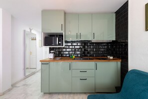 Una cocina compacta con microondas, estufa y armarios verdes.