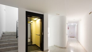 A modern interior with a marble staircase, a yellow elevator, and a clean, white hallway.