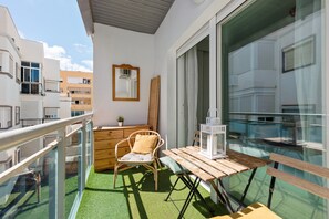 Un balcon avec une table en bois, une chaise en osier, une lanterne blanche et un miroir accroché au mur.