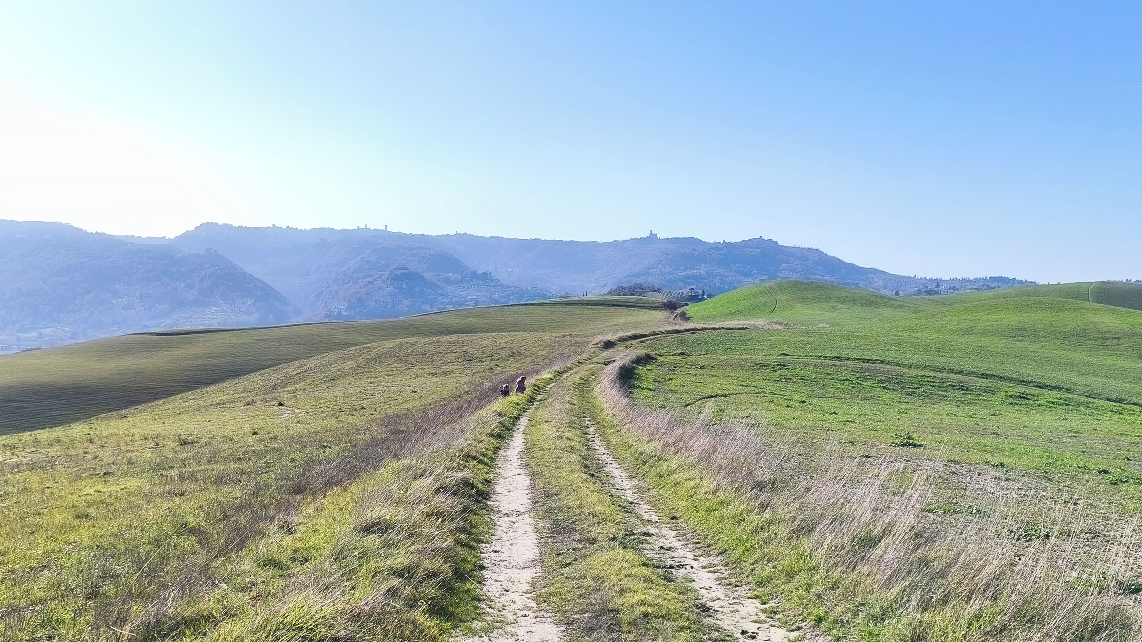 A winding dirt path through a hilly landscape with distant mountains.