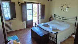 A bedroom with a bed, a radiator, a window with curtains, and a tiled floor.