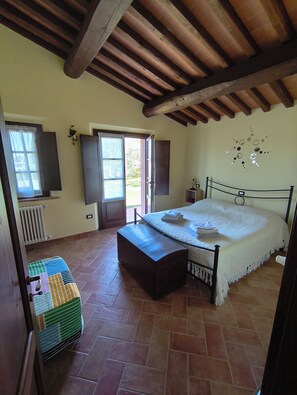 Ein Schlafzimmer mit Bett, Heizkörper, einem Fenster mit Vorhängen und einem Fliesenboden.