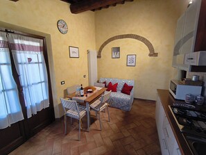 A compact kitchen with a dining table, chairs, a sofa, and a stove.