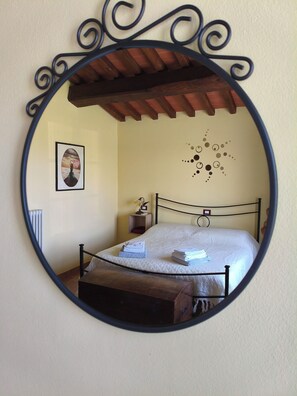 A bedroom with a bed, a bedside table, a wall-mounted mirror, and a decorative wall piece.