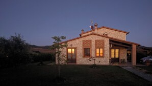 A stone house with a large window and a door, surrounded by a well-maintained lawn and a small tree.
