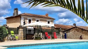Un espace piscine agrémenté d’un bâtiment en pierre, d’une porte grillagée et de chaises longues.