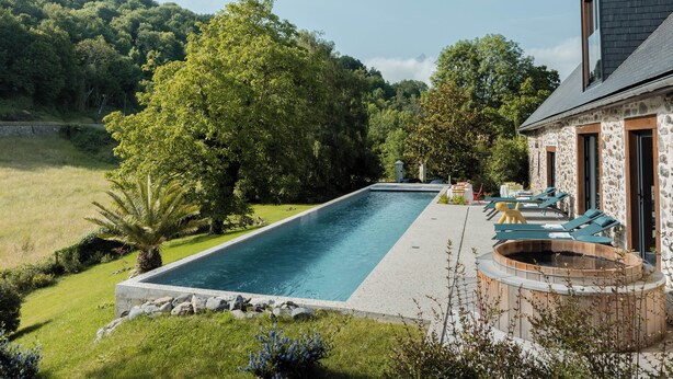 A rectangular swimming pool with a stone deck, surrounded by lush greenery and trees. There are lounge chairs and a hot tub area with a stone wall. - Lodge du Hautacam (Ayros-Arbouix)