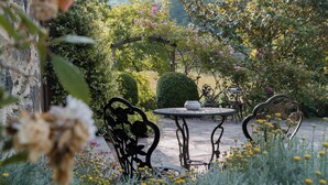 A garden patio with a round table and two chairs, surrounded by lush greenery and flowering plants. - Lodge du Hautacam (Ayros-Arbouix)