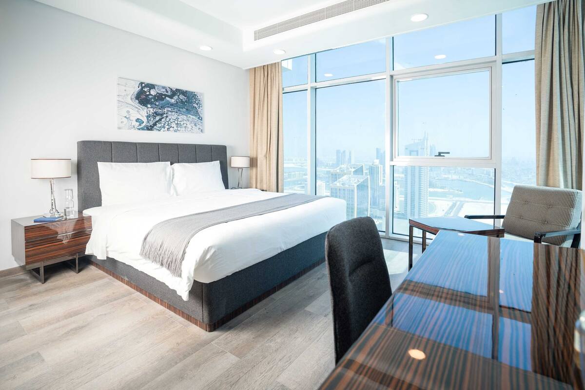 A modern hotel room with a large bed, a desk, and a view of the city.