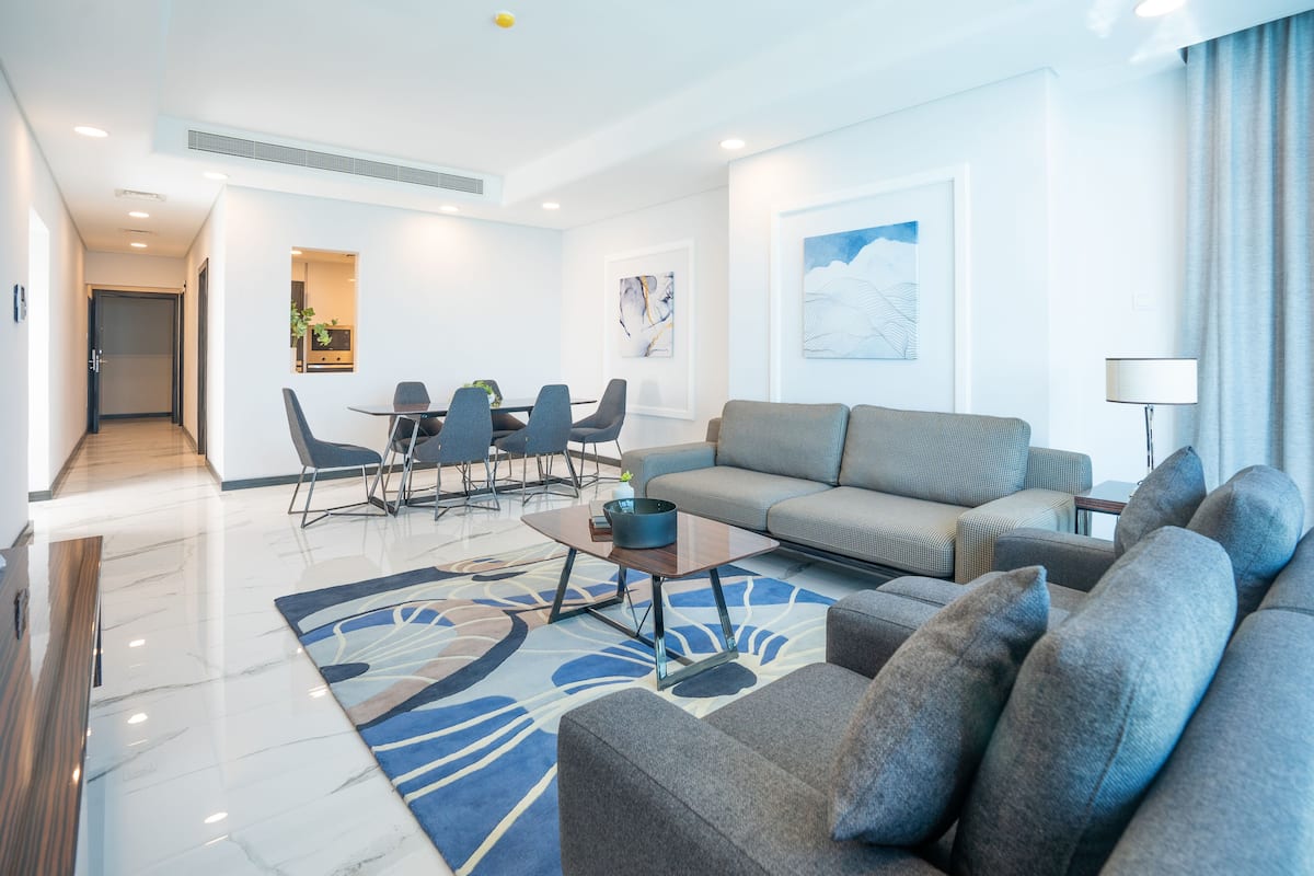 A modern living room with a grey sofa, a coffee table, and a dining area with chairs and a table.