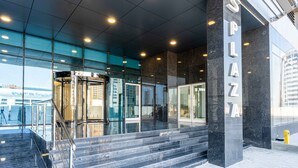 A modern building entrance with a glass facade, a name sign 'SPAZZA', and a set of stairs leading to the entrance. - S Plaza Suites Hotel (Manama)