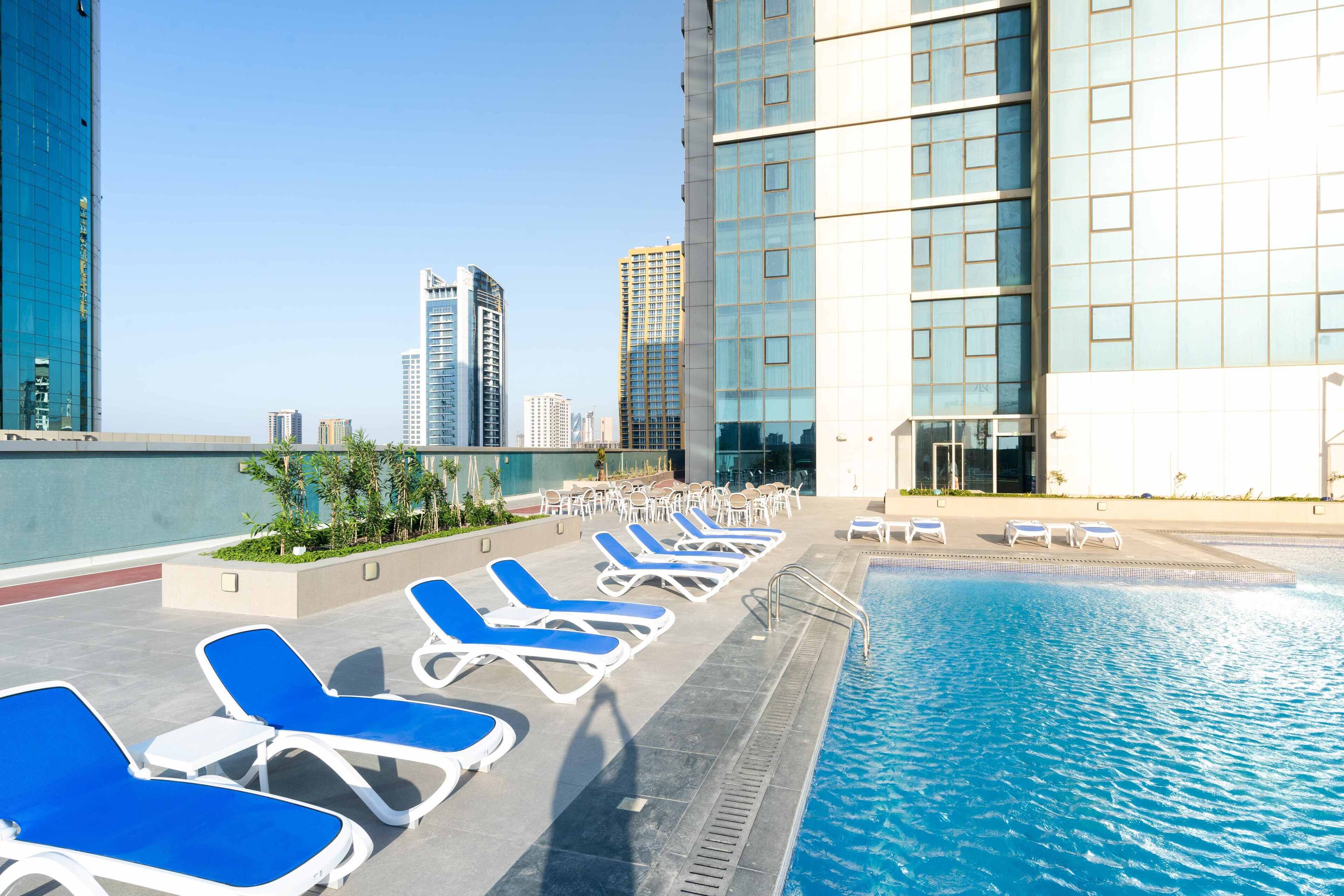 A rooftop pool area with blue lounge chairs and a view of the city skyline.