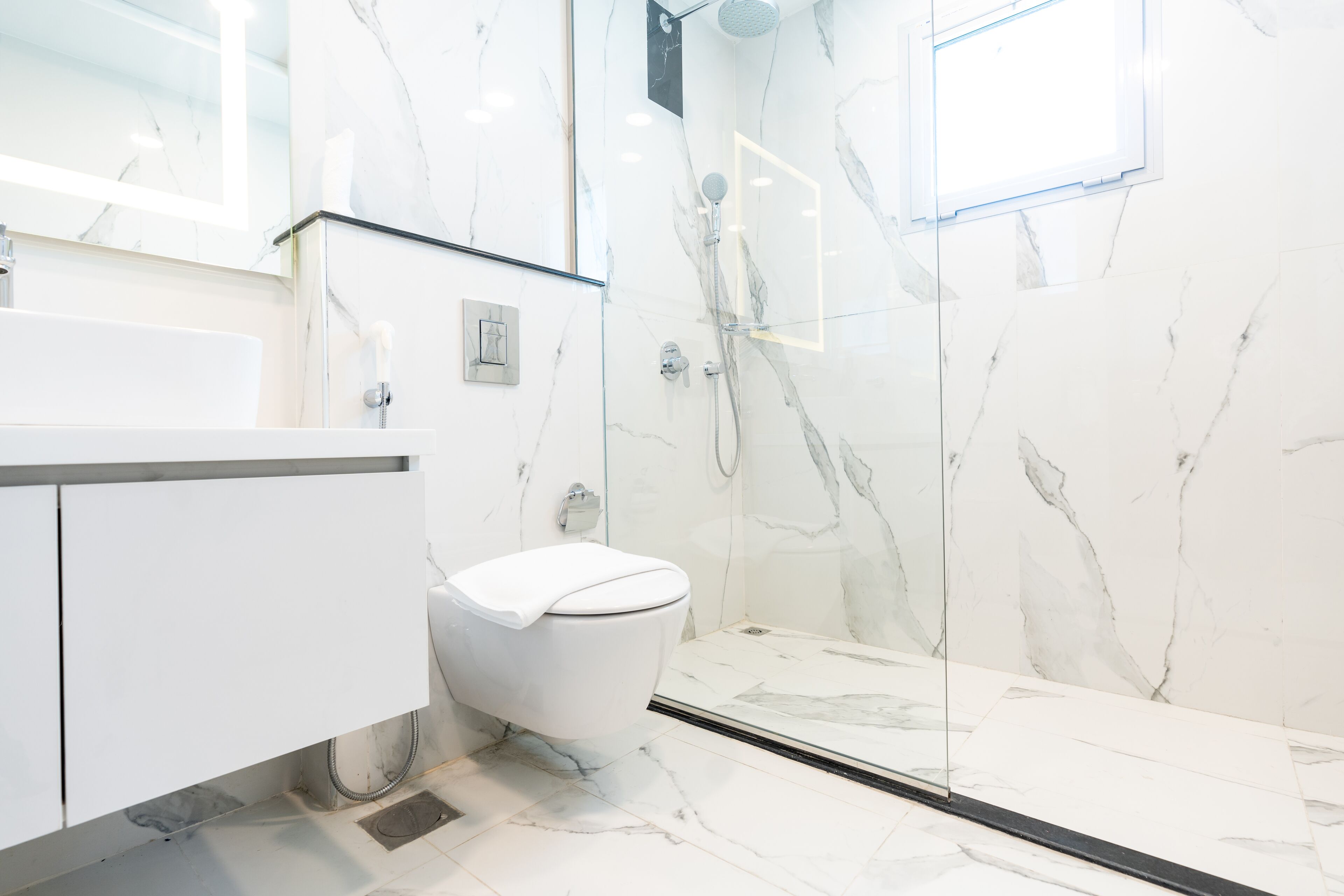 A modern bathroom with a white marble sink, a toilet, and a glass-enclosed shower area.