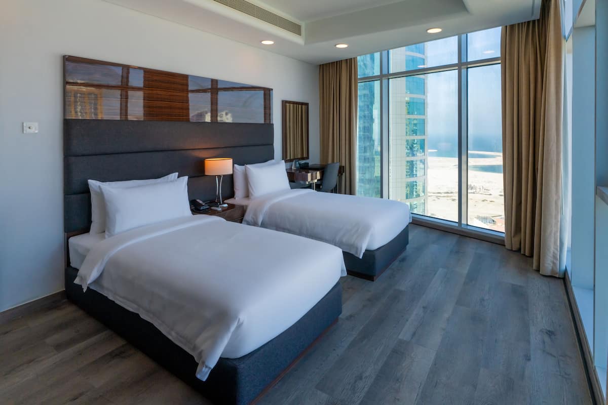 A hotel room with two beds, a large window with a view of a cityscape, and a modern design.