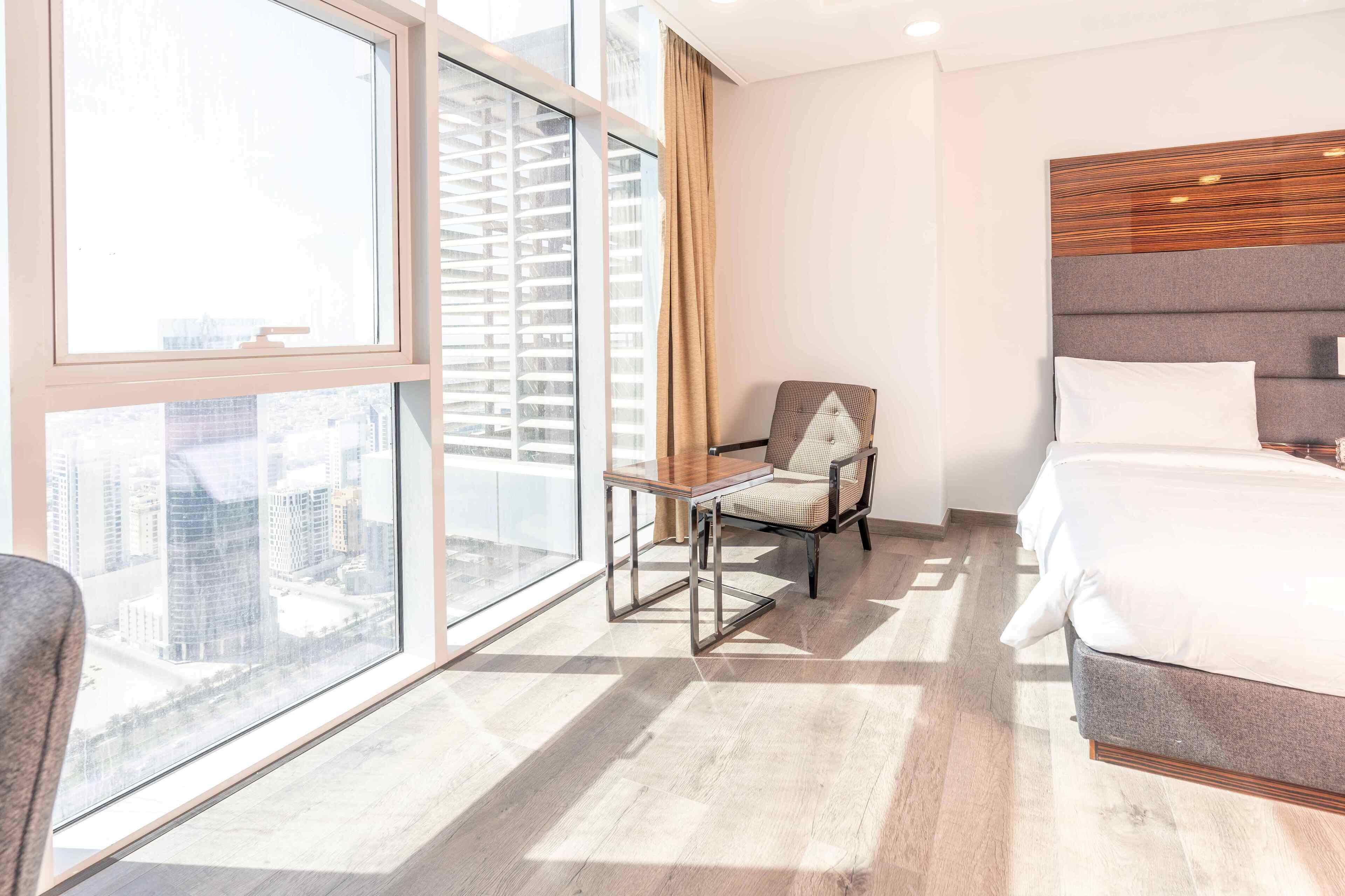 Habitación de hotel con una ventana grande, una cama, una silla y vistas a la ciudad.