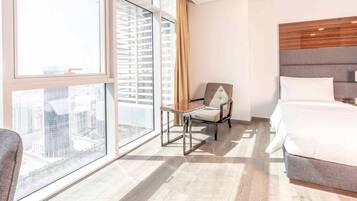 Habitación de hotel con una ventana grande, una cama, una silla y vistas a la ciudad.