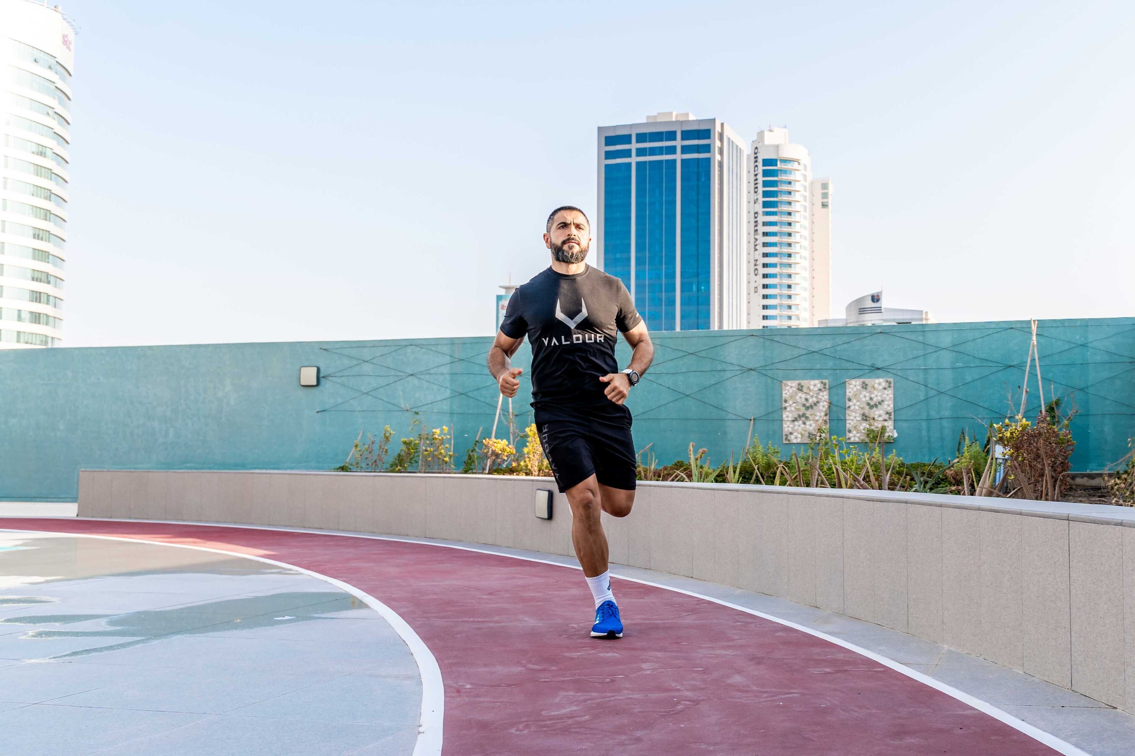 A man jogging on an outdoor track with a cityscape in the background.