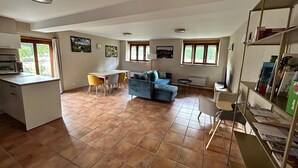 Uma sala de estar espaçosa com um sofá azul, uma mesa de jantar com cadeiras, uma cozinha com fogão e uma estante de livros.