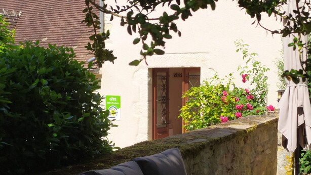 Um sofá de vime numa área de jardim com um muro de pedra, uma porta e uma placa a indicar GITE Berry Province.