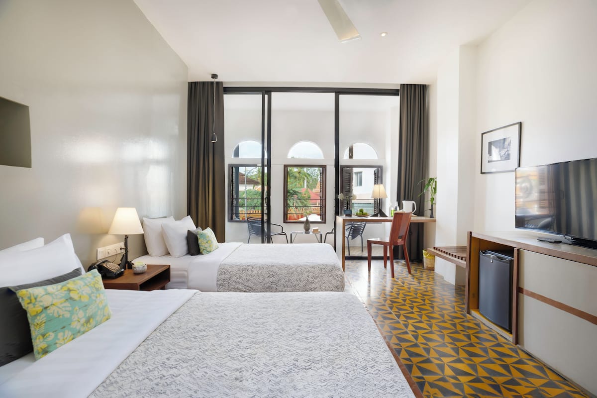 A hotel room with two beds, a desk, a television, and a balcony with a view.