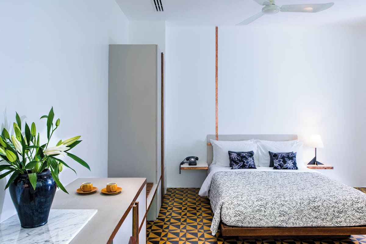 A modern hotel room with a bed, bedside table, and a potted plant.