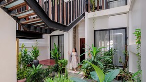 A modern interior with a staircase, potted plants, and a person standing near a doorway. - Atelier Hotel (Siem Reap)