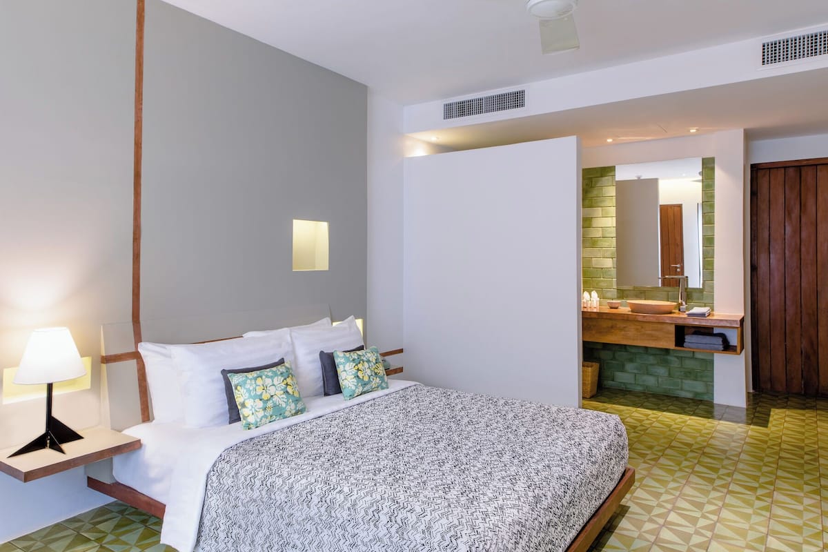 A hotel room with a bed, bedside lamp, and a bathroom with a sink and mirror.