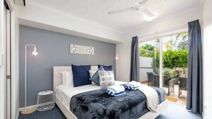 A modern bedroom with a bed, bedside lamps, a decorative wall piece, and a view of the outdoors.