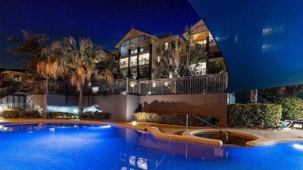 A swimming pool with a night view of a hotel, palm trees, and a well-lit building.