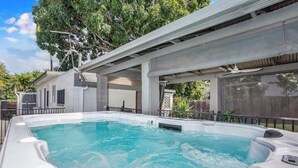A swimming pool with hot tubs, a covered patio, and a view of trees. - Seaside Serenity—Family Escape with Private Spa (Machans Beach)