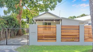 A modern house with a fenced yard, a covered porch, and a small garage. - Seaside Serenity—Family Escape with Private Spa (Machans Beach)