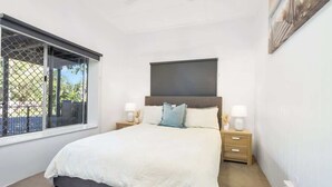 A bedroom with a bed, nightstands, a window with a view, and a ceiling fan. - Seaside Serenity—Family Escape with Private Spa (Machans Beach)