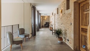 Un pasillo con pared de piedra, una puerta de madera que dice "Chambre Spacieuse" y dos sillas.