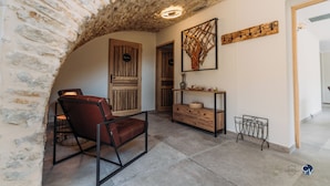 Una habitación con un arco de piedra, un armario de madera, una silla y una obra de arte colgada en la pared.