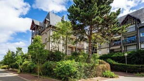 A modern multi-story building with a mix of residential and commercial spaces, surrounded by lush greenery and a cobblestone pathway. - Le Clos Mathilde by Interhome (Cabourg)