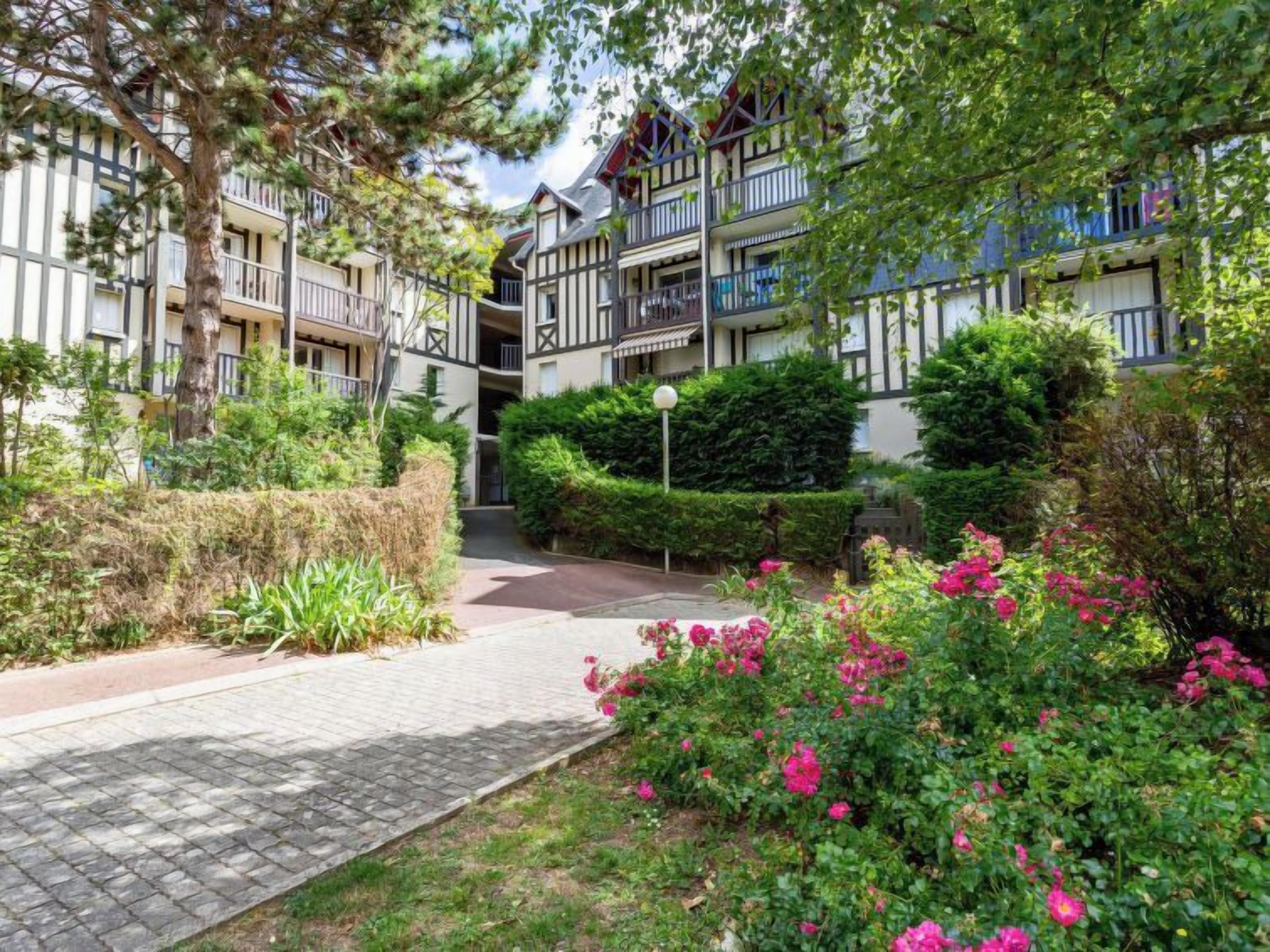 A courtyard with a paved walkway, surrounded by lush greenery and flowering plants.