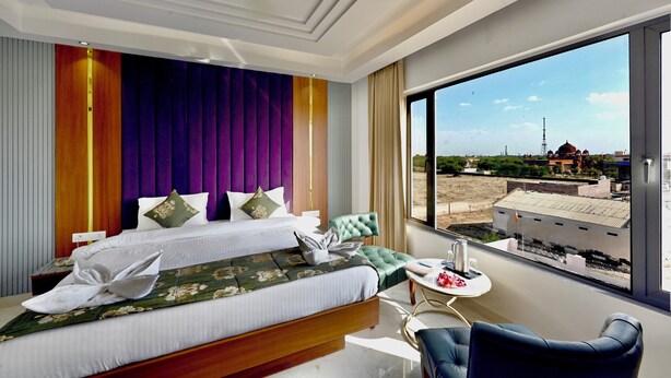 A hotel room with a large bed, a small table, a chair, and a view of the outside. - Hotel Sagar residency (Bikaner)