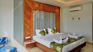 A modern hotel room with a wooden headboard, a bed with white linens, a blue chair, and a small bedside table. - Hotel Sagar residency (Bikaner)