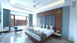 A modern bedroom with a large bed, a ceiling fan, and a view of a building outside. - Hotel Sagar residency (Bikaner)