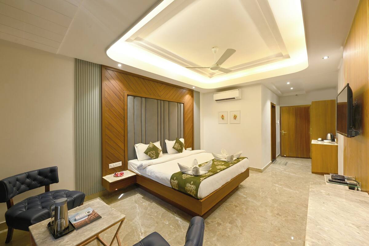 A modern hotel room with a large bed, a seating area with a coffee table, a flat-screen TV, and a ceiling fan.