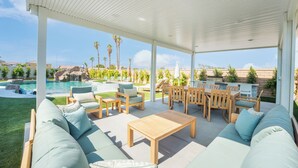 A covered outdoor seating area with a pool, lounge chairs, and a wooden table. - Rockslide House - New build, resort style pool, endless amenities (3 miles to festivals) (Coachella)