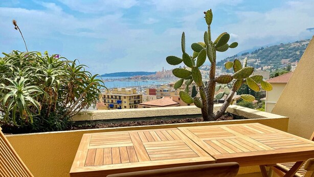 Une table et des chaises en bois sur un balcon offrant une vue sur le paysage urbain de la côte.