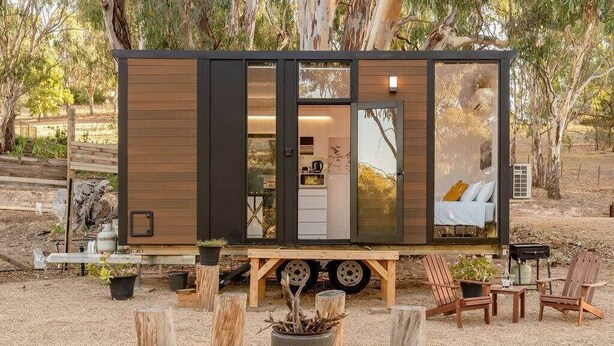 Una cabaña compacta y moderna con puerta corrediza, una pequeña cocina y una acogedora zona de estar con sillas y una mesa.